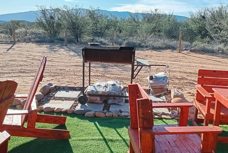 A braai stand and red timber seating on open ground with a long mountain range on the skyline