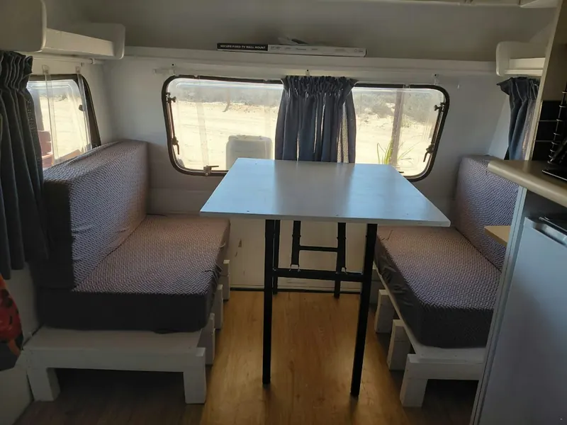 A table with bench seating on either side inside the caravan, windows on both walls