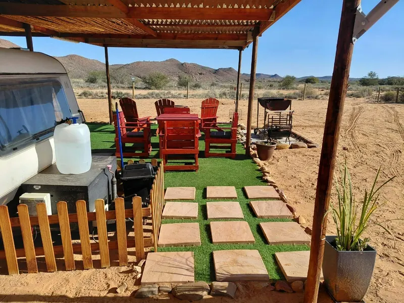 The side of the caravan with the braai, red chairs and paving stones leading across the lawn