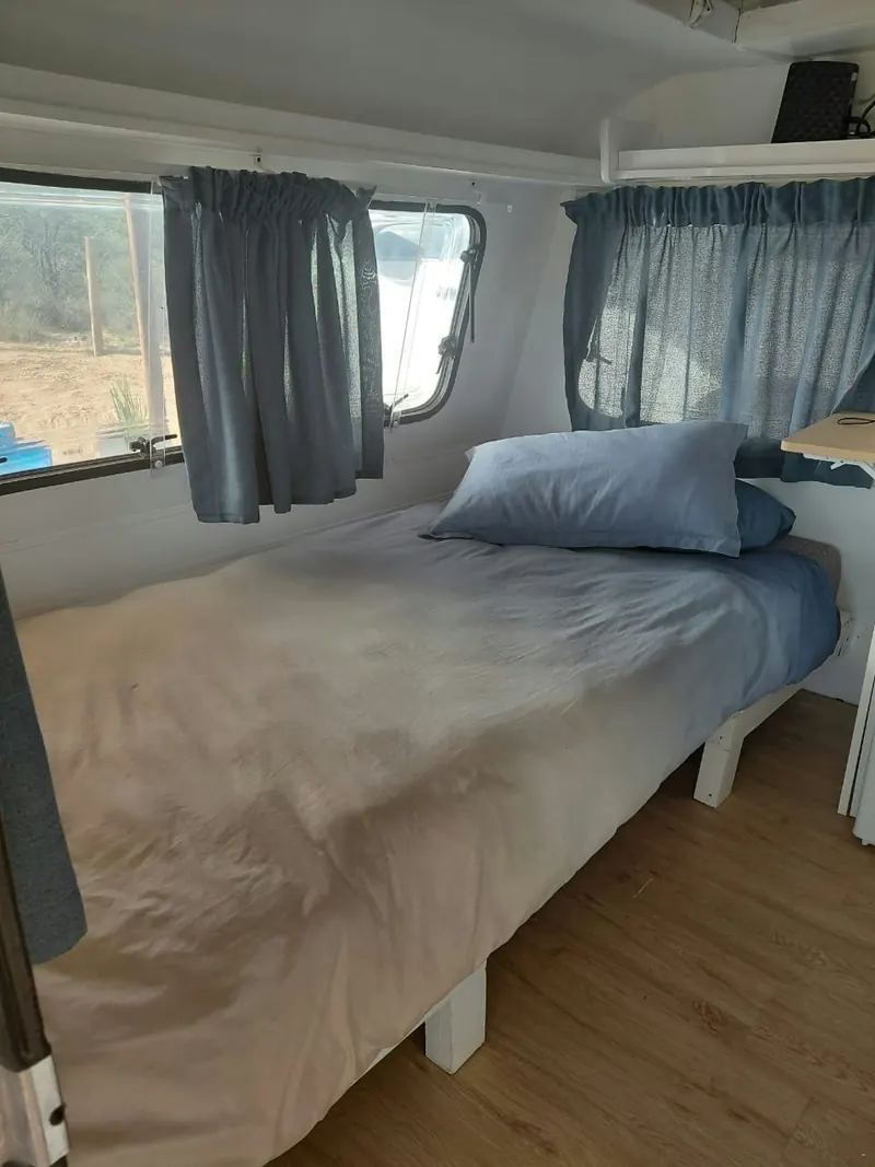A single bed made up along the wall of the caravan beneath a curtained window