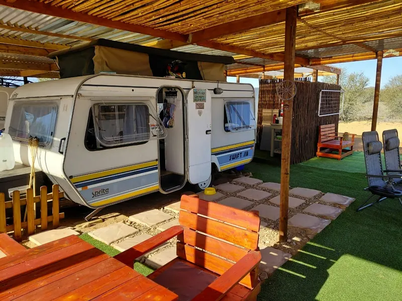 The vintage touring caravan at Karoo Stone Camper parked under a timber and reed pergola with red slatted chairs in front of it
