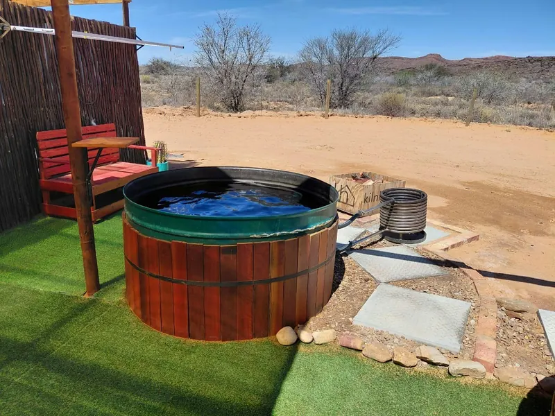 A filled wood-fired hot tub beside a red swing bench at Karoo Stone Camper