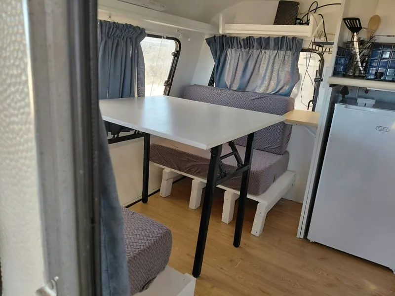 The kitchenette end of the caravan with a bar fridge, utensils and the fold-out table