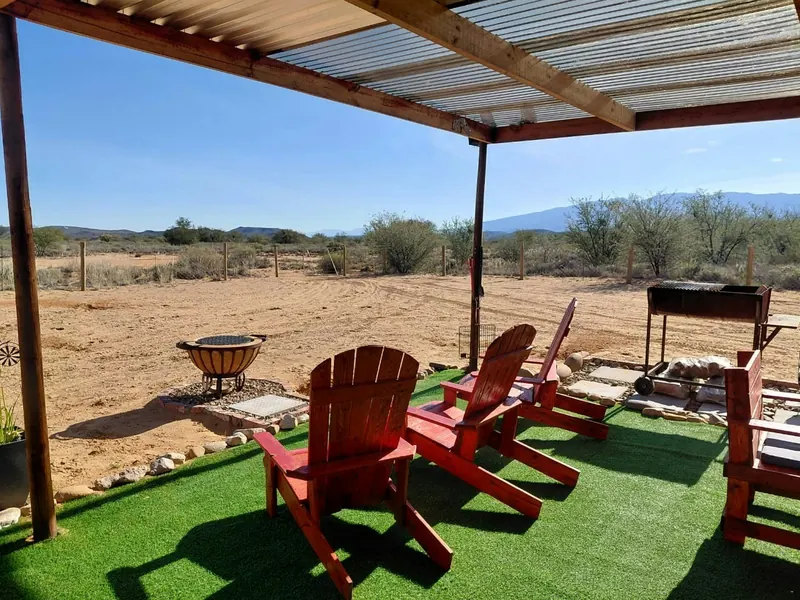 Red chairs, a firepit and a braai on open ground with the Karoo plain and low hills beyond