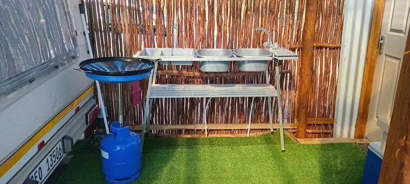 A double dishwashing stand with two metal basins set up outside next to the caravan and a gas bottle