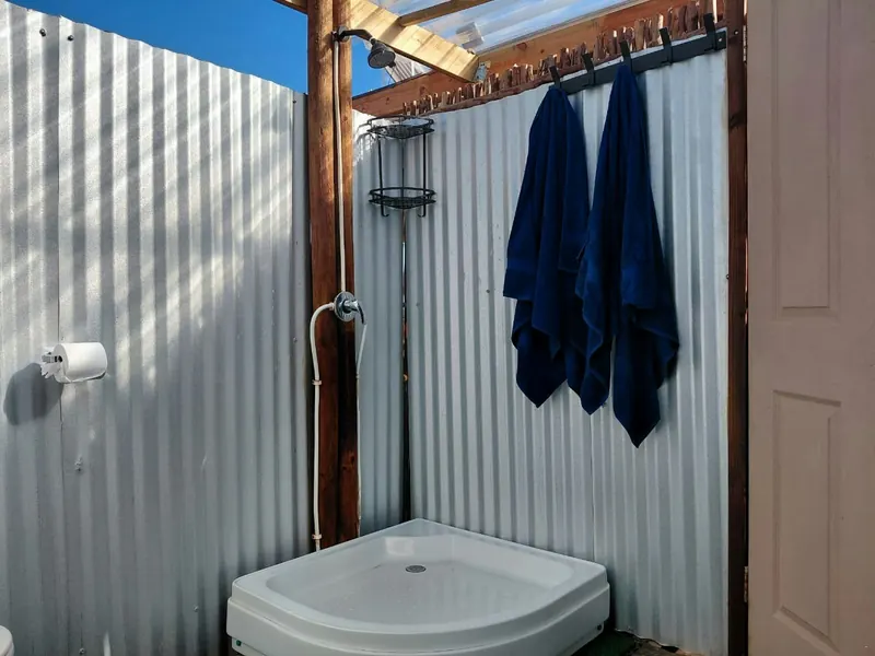 An outdoor shower with a corner tray, a rail with two navy towels hanging, inside a corrugated enclosure