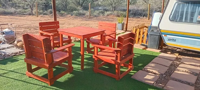 A red painted outdoor dining table and four matching chairs standing on lawn beside the caravan