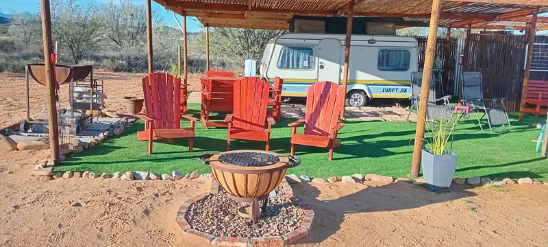 The shaded outdoor lounge with red chairs around the firepit at Karoo Stone Camper